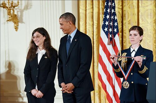 Former President Barack Obama looks at May Berenbaum as a woman in a military uniform holds the National Medal of Science