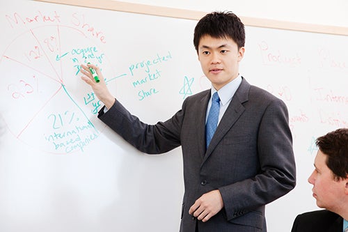 A student in a suit makes a presentation on a white board