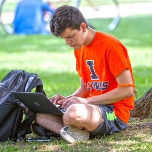 Student working on computer sitting under a tree on the Quad